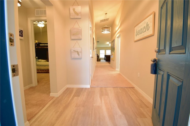 hallway featuring light wood-type flooring, baseboards, and visible vents