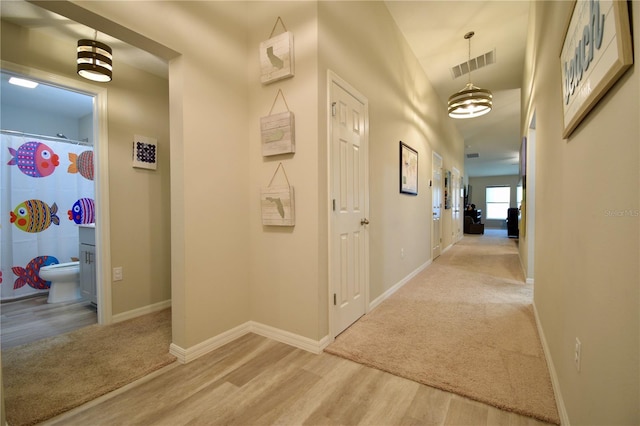 hall with light wood-style floors, baseboards, visible vents, and light colored carpet