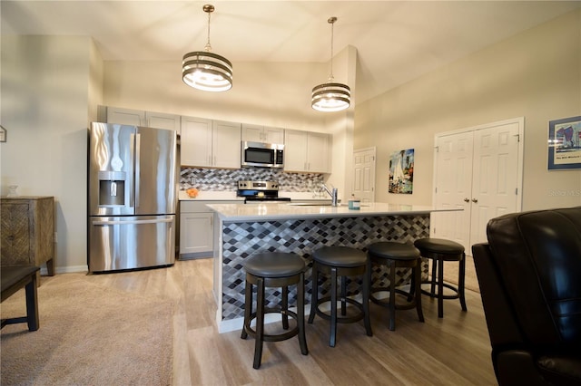 kitchen featuring a breakfast bar area, light wood-style floors, light countertops, appliances with stainless steel finishes, and tasteful backsplash