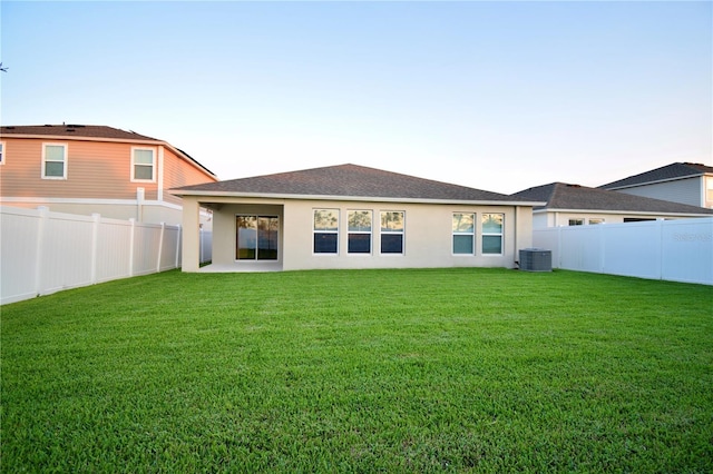 back of property with stucco siding, a fenced backyard, central AC, and a yard