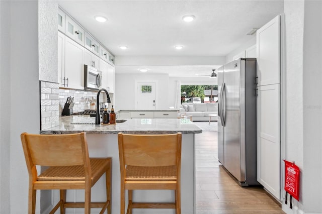 kitchen featuring decorative backsplash, light stone counters, a peninsula, stainless steel appliances, and light wood-type flooring