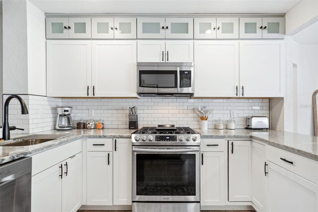 kitchen featuring white cabinets, appliances with stainless steel finishes, backsplash, and a sink