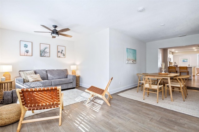 living room featuring a ceiling fan, baseboards, and wood finished floors