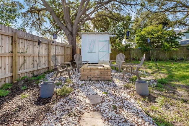 view of yard featuring an outdoor fire pit, a fenced backyard, a storage unit, and an outbuilding