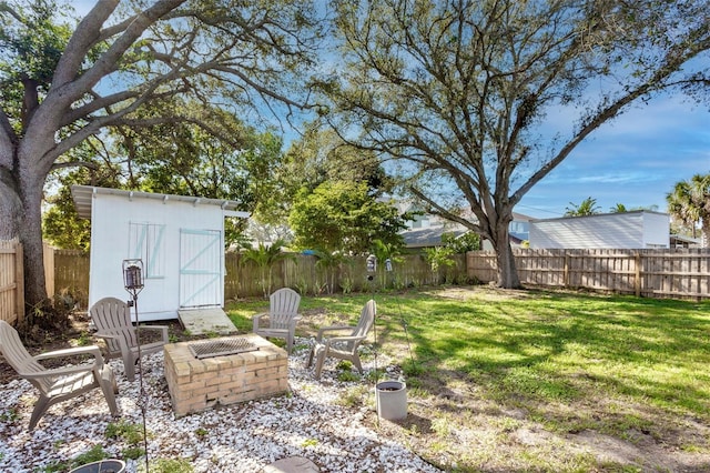 view of yard with an outdoor fire pit, a fenced backyard, an outbuilding, and a storage unit