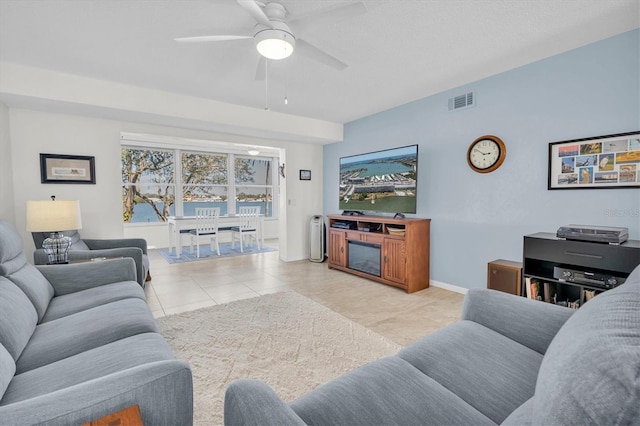 living area featuring a fireplace, visible vents, a ceiling fan, tile patterned flooring, and baseboards