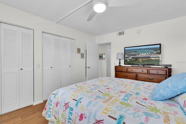 bedroom with a ceiling fan, visible vents, two closets, and wood finished floors