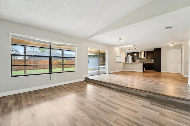 unfurnished living room with visible vents, a textured ceiling, light wood-type flooring, and baseboards