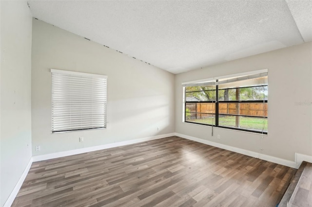 empty room featuring baseboards, a textured ceiling, wood finished floors, and vaulted ceiling