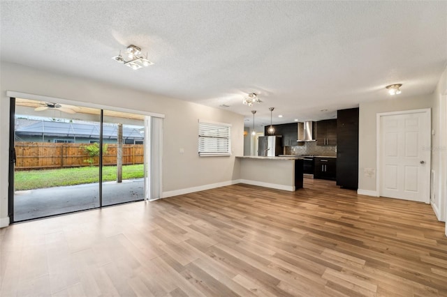 unfurnished living room featuring light wood-type flooring, baseboards, and a textured ceiling