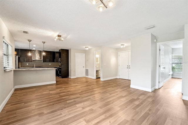 unfurnished living room with visible vents, baseboards, a textured ceiling, and light wood-style flooring