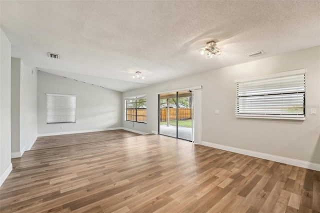 spare room featuring visible vents, lofted ceiling, a textured ceiling, and wood finished floors