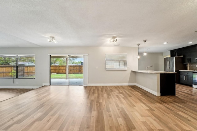 unfurnished living room featuring a textured ceiling, light wood-type flooring, baseboards, and a sink