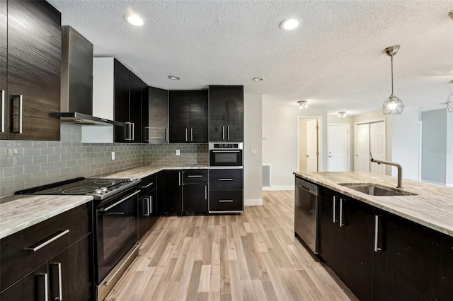 kitchen with a sink, dark cabinetry, appliances with stainless steel finishes, wall chimney exhaust hood, and decorative backsplash