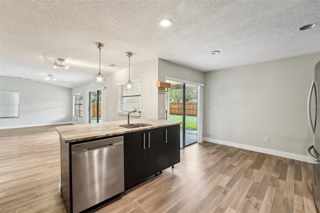 kitchen with light wood-style flooring, a sink, open floor plan, appliances with stainless steel finishes, and dark cabinets