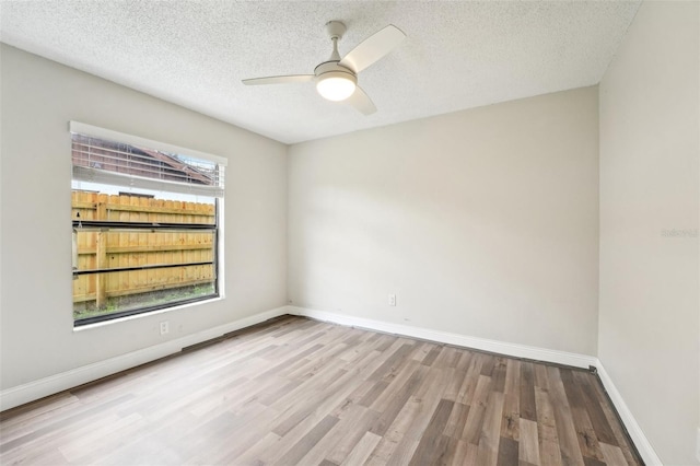 empty room with baseboards, a textured ceiling, wood finished floors, and a ceiling fan