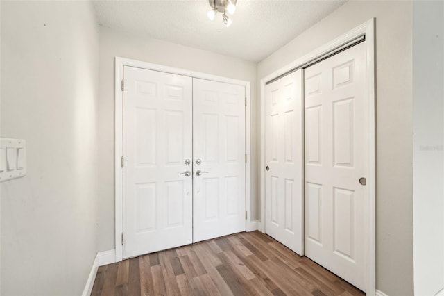 unfurnished bedroom featuring a closet, baseboards, a textured ceiling, and wood finished floors