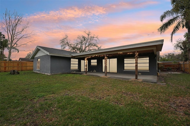 rear view of house with a yard, a fenced backyard, stucco siding, and a patio area