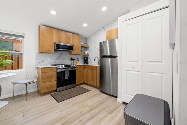 kitchen with a sink, light wood-style floors, light countertops, appliances with stainless steel finishes, and decorative backsplash