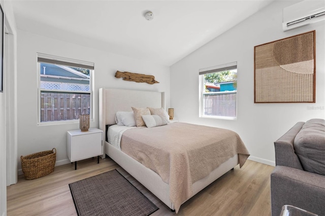 bedroom with lofted ceiling, light wood-style floors, baseboards, and an AC wall unit