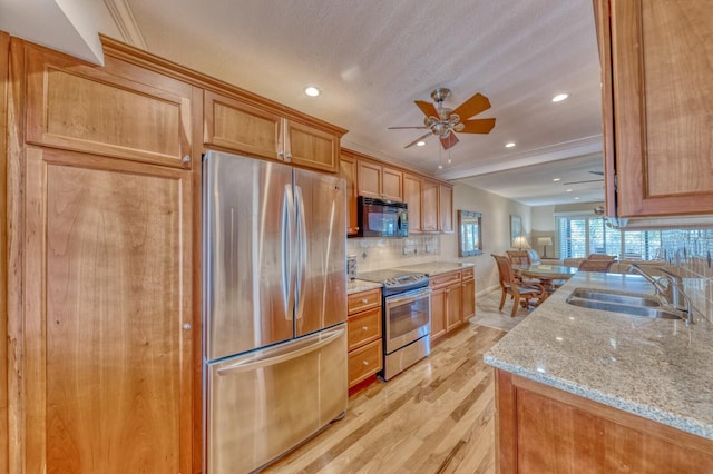 kitchen featuring light stone counters, tasteful backsplash, light wood-style flooring, appliances with stainless steel finishes, and a sink