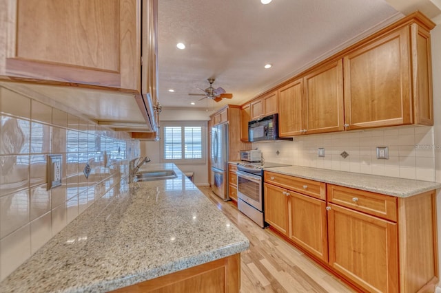 kitchen featuring light wood finished floors, stainless steel appliances, tasteful backsplash, a sink, and ceiling fan