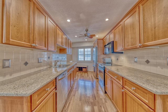 kitchen with a sink, a ceiling fan, light wood-style floors, appliances with stainless steel finishes, and light stone countertops