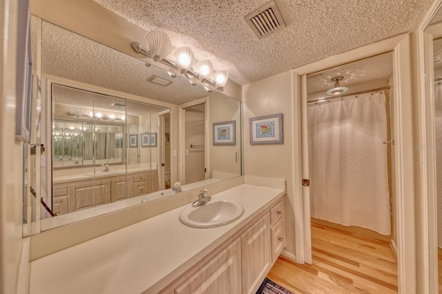 full bathroom with visible vents, a textured ceiling, vanity, and wood finished floors