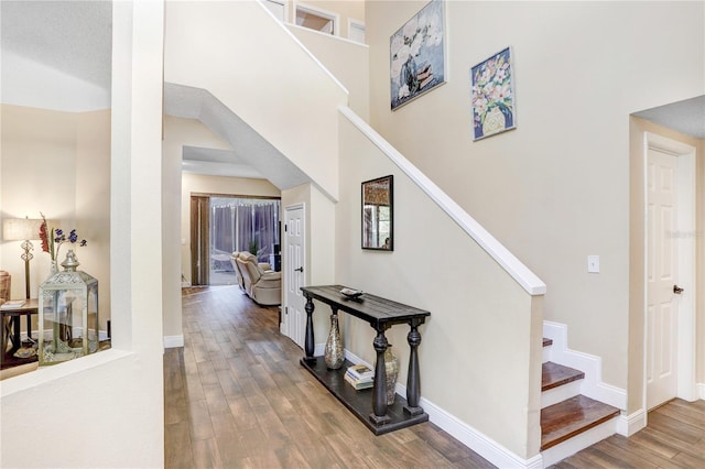 hallway with a high ceiling, stairs, baseboards, and wood finished floors