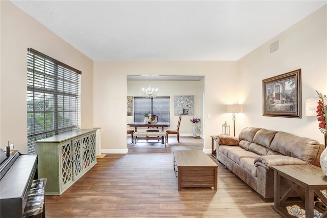 living area featuring visible vents, a notable chandelier, baseboards, and wood finished floors