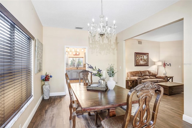 dining space featuring baseboards, visible vents, an inviting chandelier, and wood finished floors