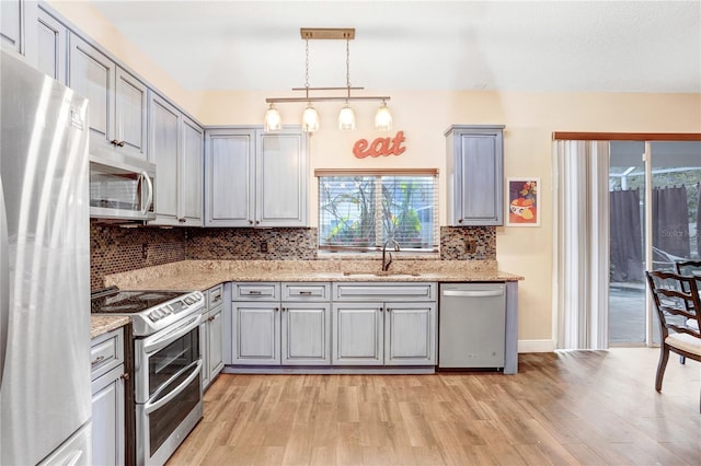 kitchen featuring light wood finished floors, decorative backsplash, gray cabinets, stainless steel appliances, and a sink