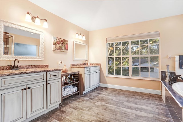 bathroom with a relaxing tiled tub, vanity, baseboards, and wood finished floors