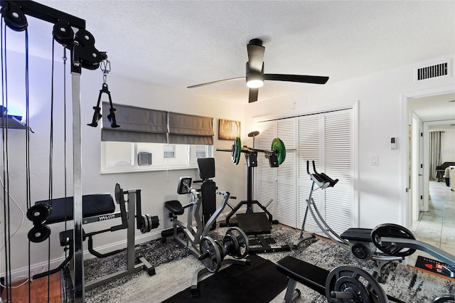 exercise area featuring a ceiling fan, visible vents, a textured ceiling, and baseboards