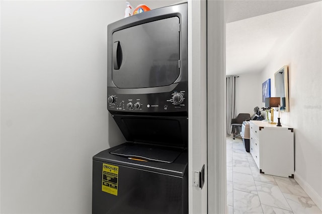 clothes washing area featuring marble finish floor, baseboards, laundry area, and stacked washer / dryer