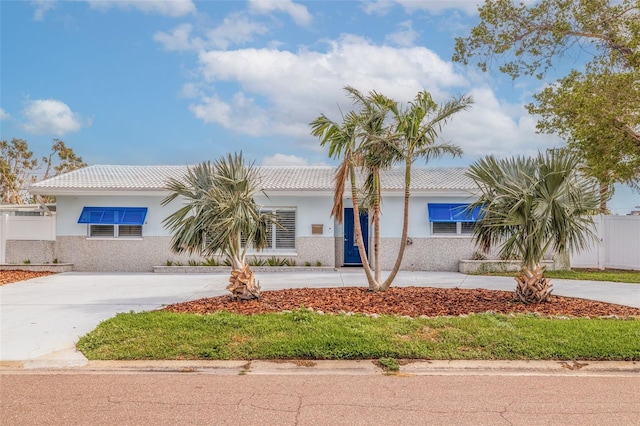 view of front facade with stucco siding, a tile roof, concrete driveway, and fence