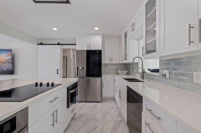 kitchen featuring marble finish floor, black appliances, a sink, a barn door, and white cabinets