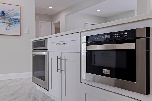 kitchen with oven, baseboards, marble finish floor, and white cabinetry