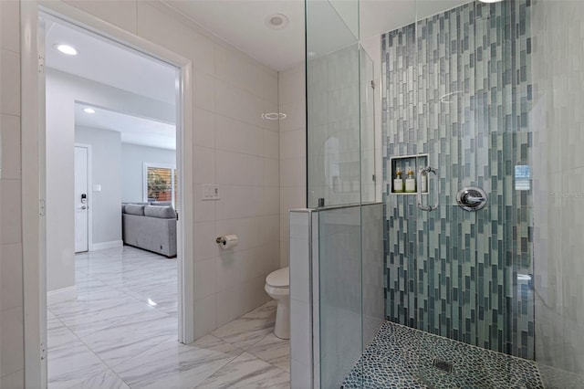 full bathroom with tiled shower, toilet, marble finish floor, and tile walls