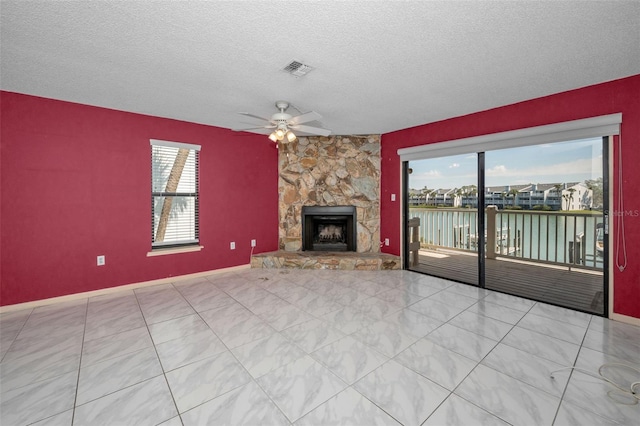 unfurnished living room featuring ceiling fan, a textured ceiling, a stone fireplace, a water view, and visible vents