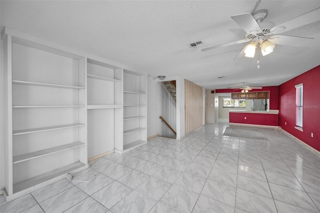 interior space featuring a ceiling fan, visible vents, a textured ceiling, and stairs