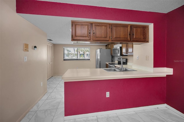 kitchen featuring brown cabinetry, a peninsula, stainless steel appliances, light countertops, and a sink