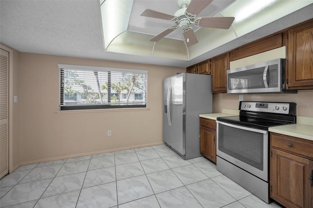 kitchen with baseboards, brown cabinetry, stainless steel appliances, a textured ceiling, and light countertops