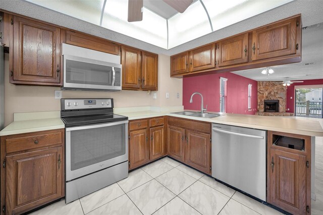 kitchen with ceiling fan, appliances with stainless steel finishes, brown cabinets, a peninsula, and a sink