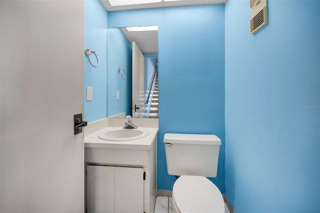 half bath with toilet, vanity, visible vents, and baseboards