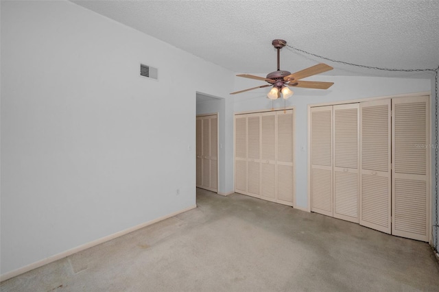 unfurnished bedroom with lofted ceiling, a textured ceiling, two closets, and visible vents