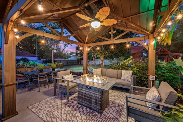 patio terrace at dusk featuring an outdoor living space with a fire pit, fence, a gazebo, a playground, and outdoor dining space