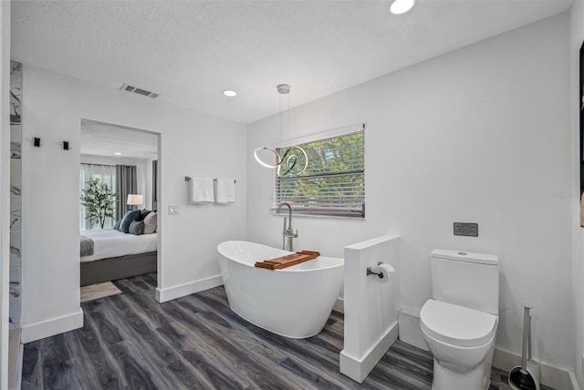 ensuite bathroom with visible vents, toilet, wood finished floors, a freestanding tub, and baseboards