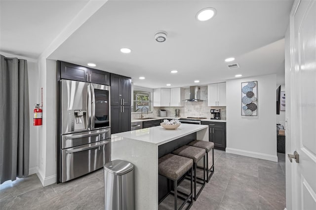 kitchen featuring light countertops, decorative backsplash, appliances with stainless steel finishes, a sink, and wall chimney range hood