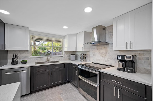 kitchen featuring stainless steel appliances, decorative backsplash, white cabinetry, a sink, and wall chimney exhaust hood